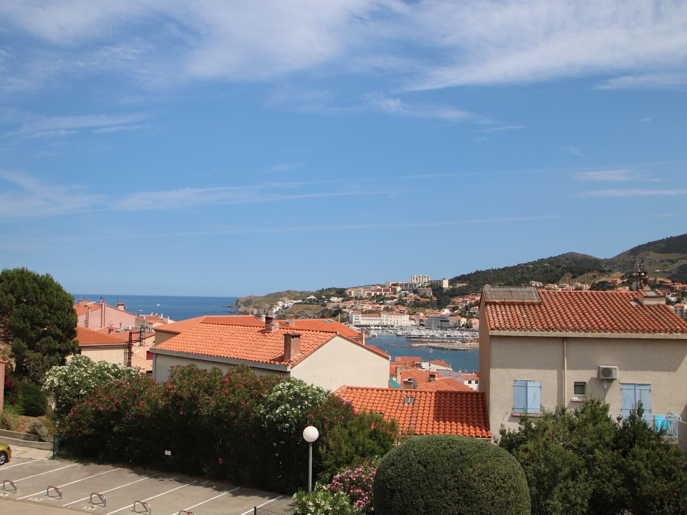 A coastal town with red-roofed buildings, a marina, and a clear blue sky.