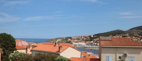A coastal town with red-roofed buildings, a marina, and a clear blue sky.
