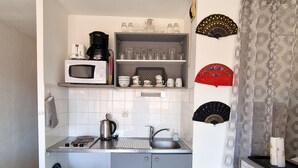 Een praktische keuken met een magnetron, waterkoker en koffiezetapparaat op het aanrecht, een spoelbak en een klein prullenbakje.