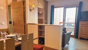 Ett kompakt bostadsutrymme med matplats, litet kök och en skjutdörr som leder ut till en balkong.