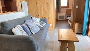 Ett mysigt rum med en grå soffa, träväggar, ett träbord och en liten säng i bakgrunden.