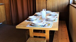 A wooden dining table set with white plates, bowls, and a pitcher, accompanied by placemats with floral designs. - Cozy 2-Room Mountain Apartment for 5 in the Heart of Vars, Near Slopes and Shops (Vars)