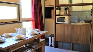 A compact kitchen with a microwave, sink, and wooden cabinets. A dining table with plates and a pitcher is set up near a window with red curtains. - Cozy 2-Room Mountain Apartment for 5 in the Heart of Vars, Near Slopes and Shops (Vars)