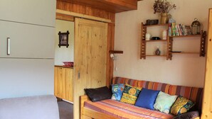 A cozy room with a wooden sofa, a small bed, a wooden cabinet, and a shelf with books and a lantern. - Cozy 2-Room Mountain Apartment for 5 in the Heart of Vars, Near Slopes and Shops (Vars)