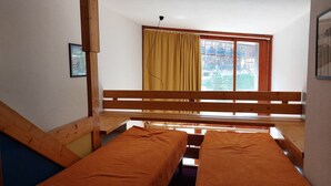 A small, cozy room with two wooden beds, a window with curtains, and a view of buildings outside. - Renovated duplex, pets allowed, for 5 near slopes and shops (Les Arcs 1800)