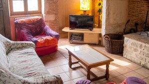 Una sala de estar con sofá, sillón, televisor, lámpara, chimenea y pared de piedra.