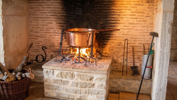 Una chimenea con una olla de cobre, leña y un cesto de astillas.
