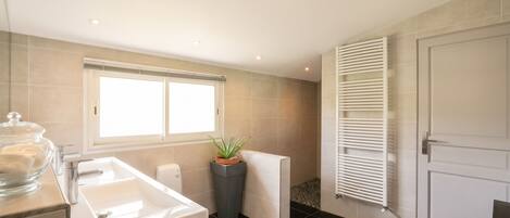 A modern bathroom with a bathtub, a window, a potted plant, and a radiator.