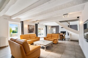A spacious living area with a sofa, armchair, and coffee table. A staircase leads to an upper level with a dining area.