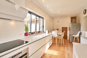 A modern kitchen with a built-in oven, a dining area with a wooden table and chairs, and a refrigerator.