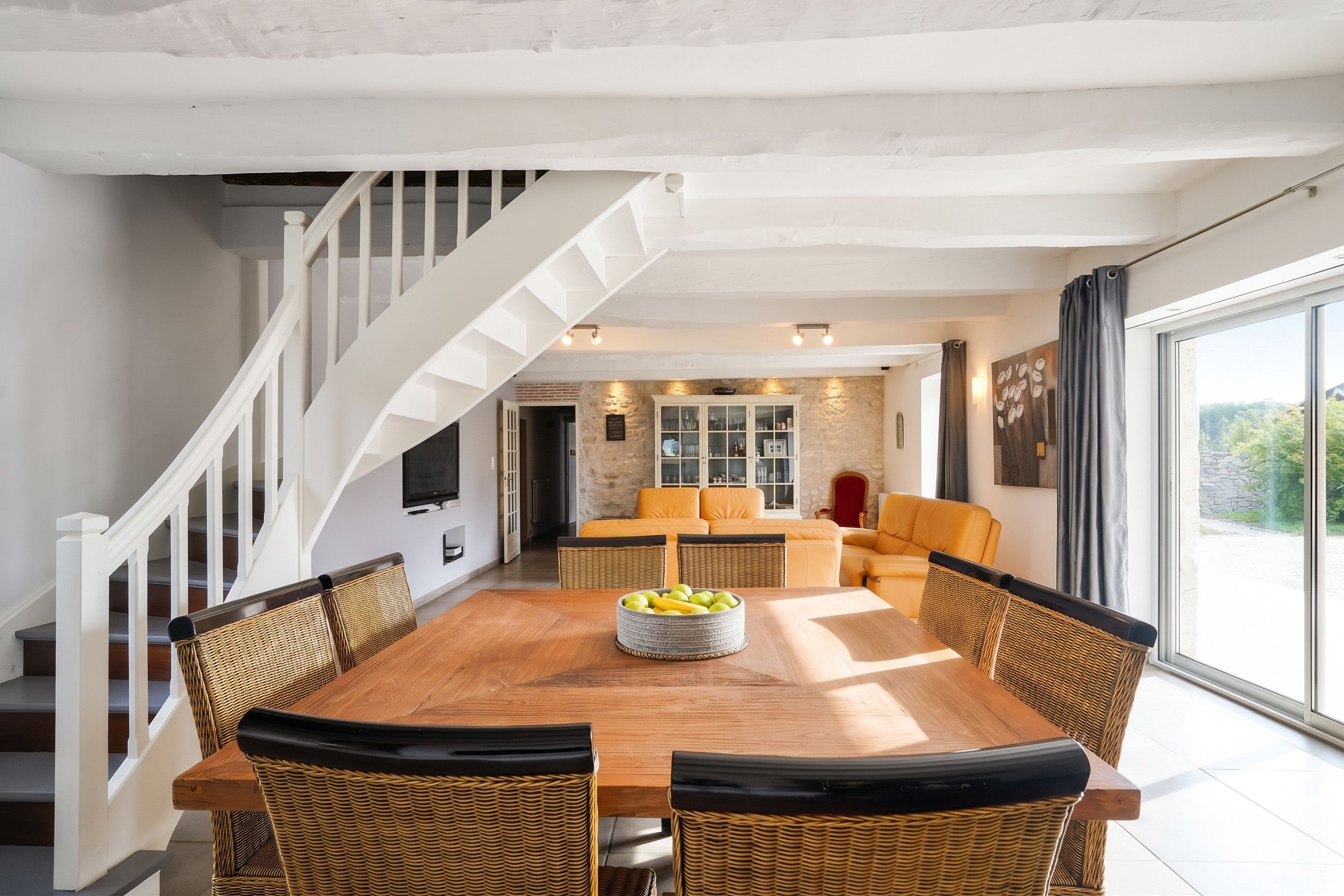 A dining area with a wooden table, wicker chairs, and a fruit bowl.