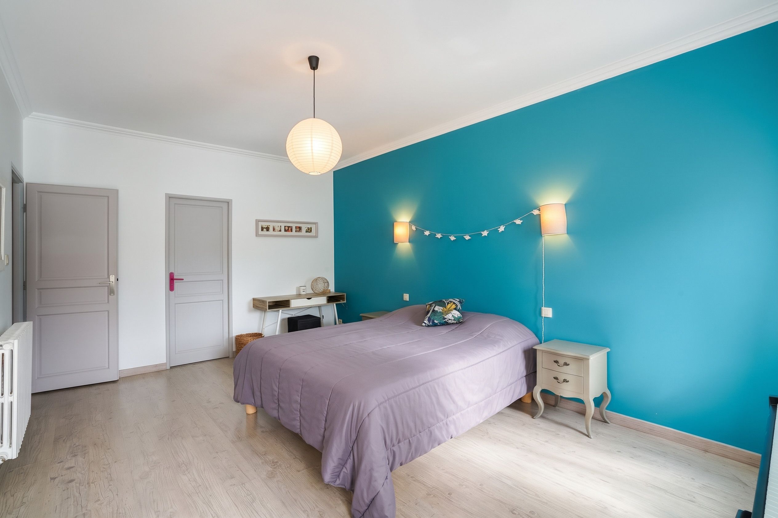 Un dormitorio con una cama, un escritorio, una silla, una lámpara y una pared decorada con luces.