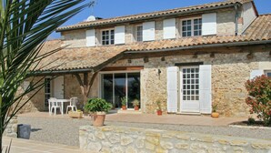 A stone building with a tiled roof, a covered patio with outdoor seating, and potted plants.