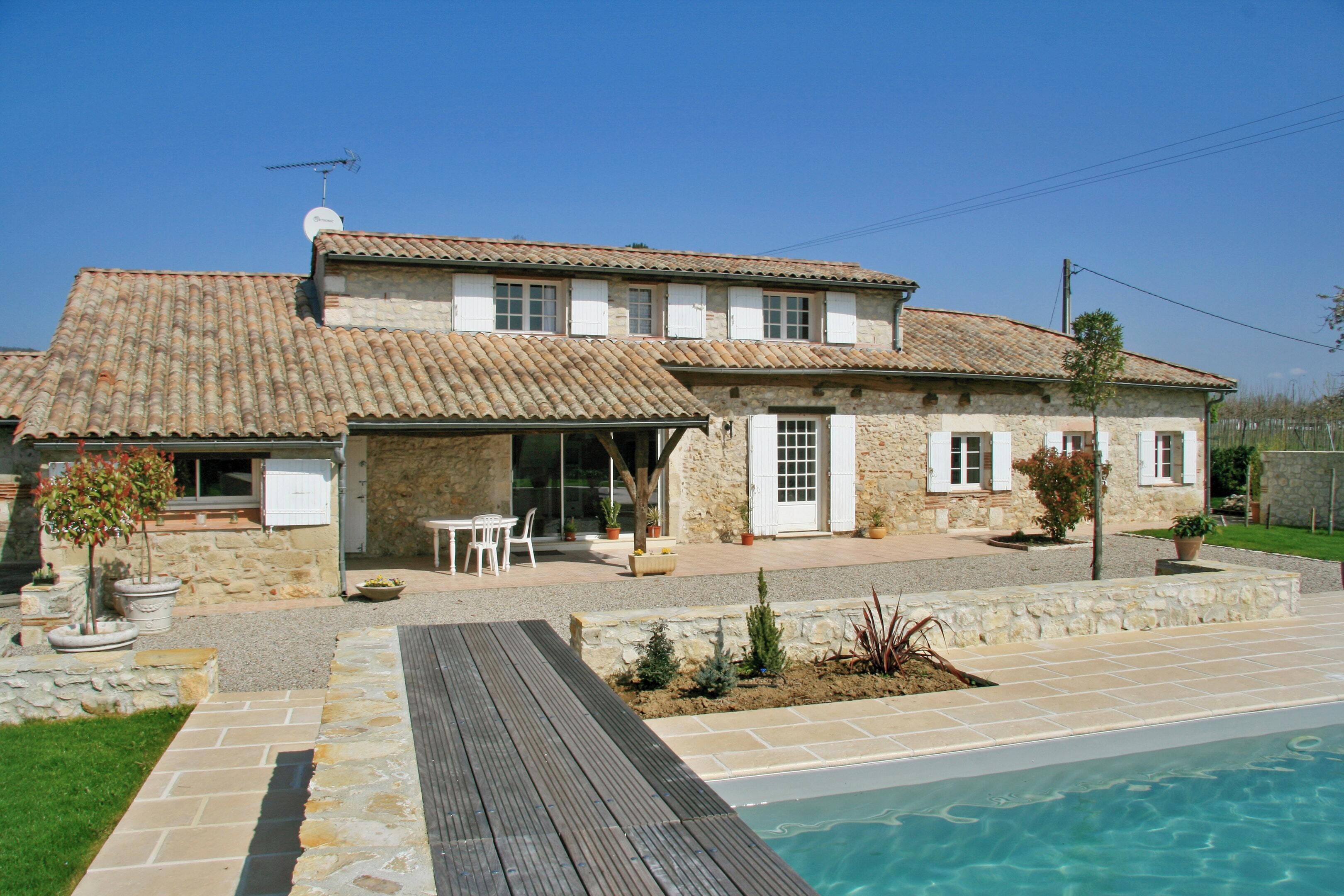 Une maison en pierre à deux étages, avec un toit en tuiles, une piscine et un patio aménagé avec du mobilier d’extérieur.