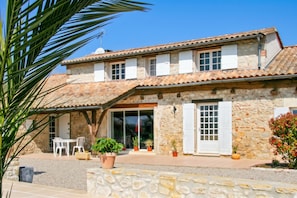 A stone building with a tiled roof, multiple windows, and a covered patio area with outdoor seating.