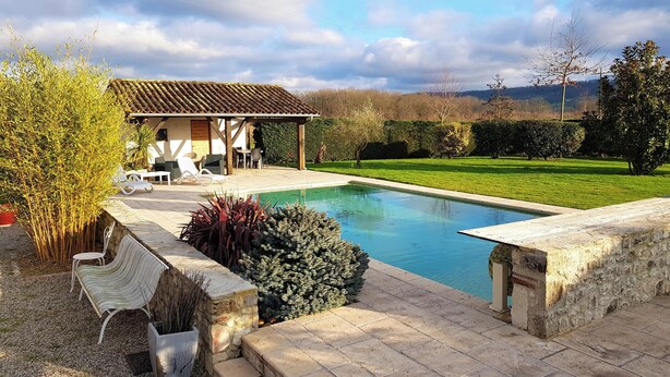 A pool area with a pergola, seating, and a view of the countryside.