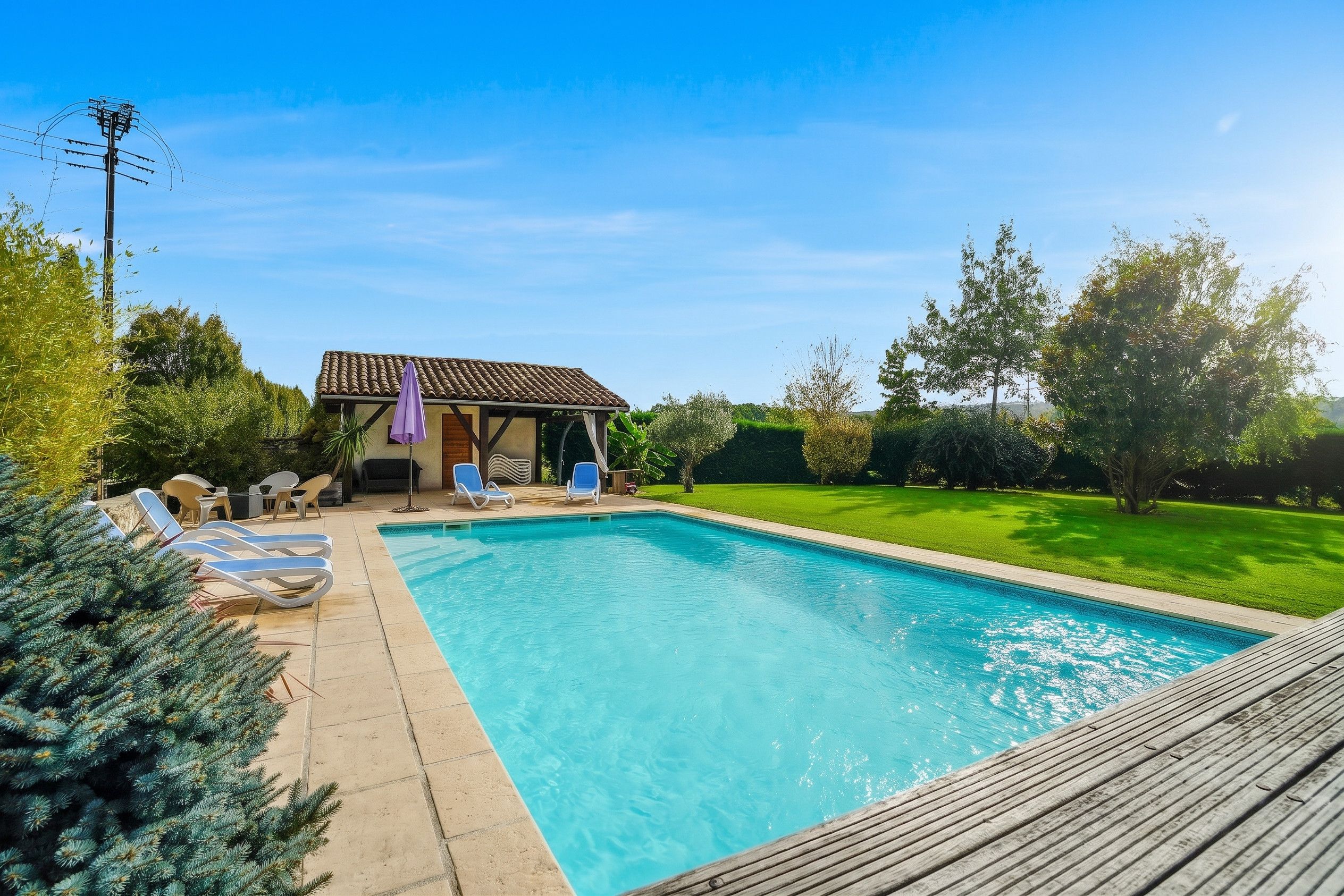 A swimming pool with lounge chairs, a covered patio, and a house with a tiled roof.