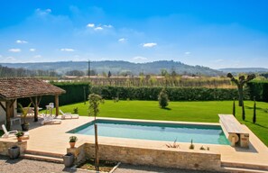A swimming pool with a stone deck, surrounded by a well-maintained lawn and a view of distant hills.