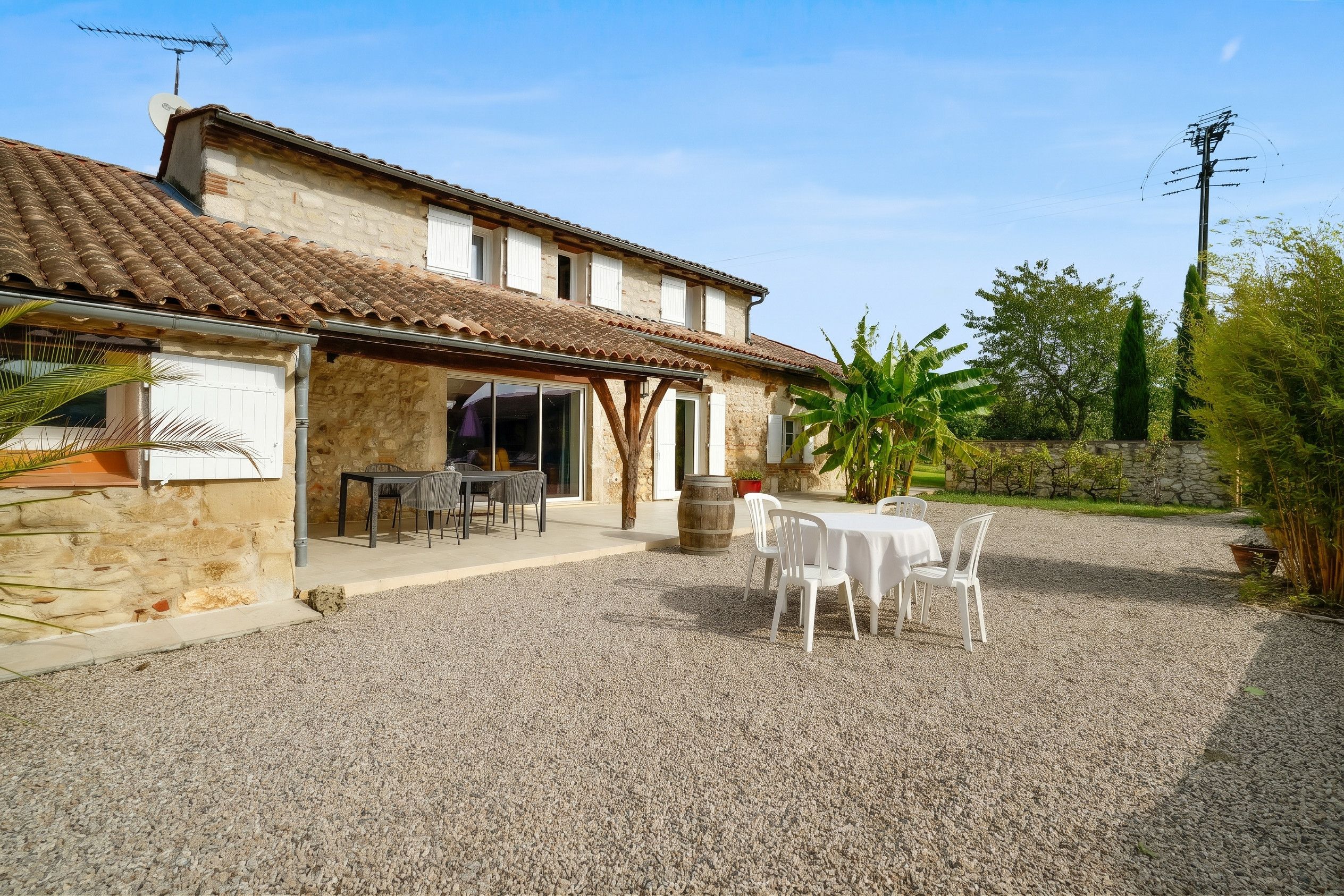 A stone building with a tiled roof, a gravel patio, and outdoor seating.