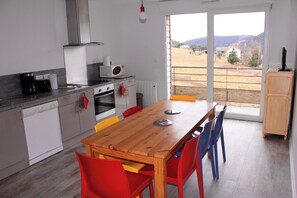 Een moderne keuken met een houten eettafel, rode en blauwe stoelen, en uitzicht op een landelijk landschap door grote ramen.