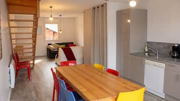 Une cuisine moderne avec une table à manger en bois et des chaises colorées, un four encastré et une machine à café.