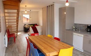 A modern kitchen with a wooden dining table and colorful chairs, a built-in oven, and a coffee maker. - Homerez - Apartment in Xonrupt-Longemer (Xonrupt-Longemer)