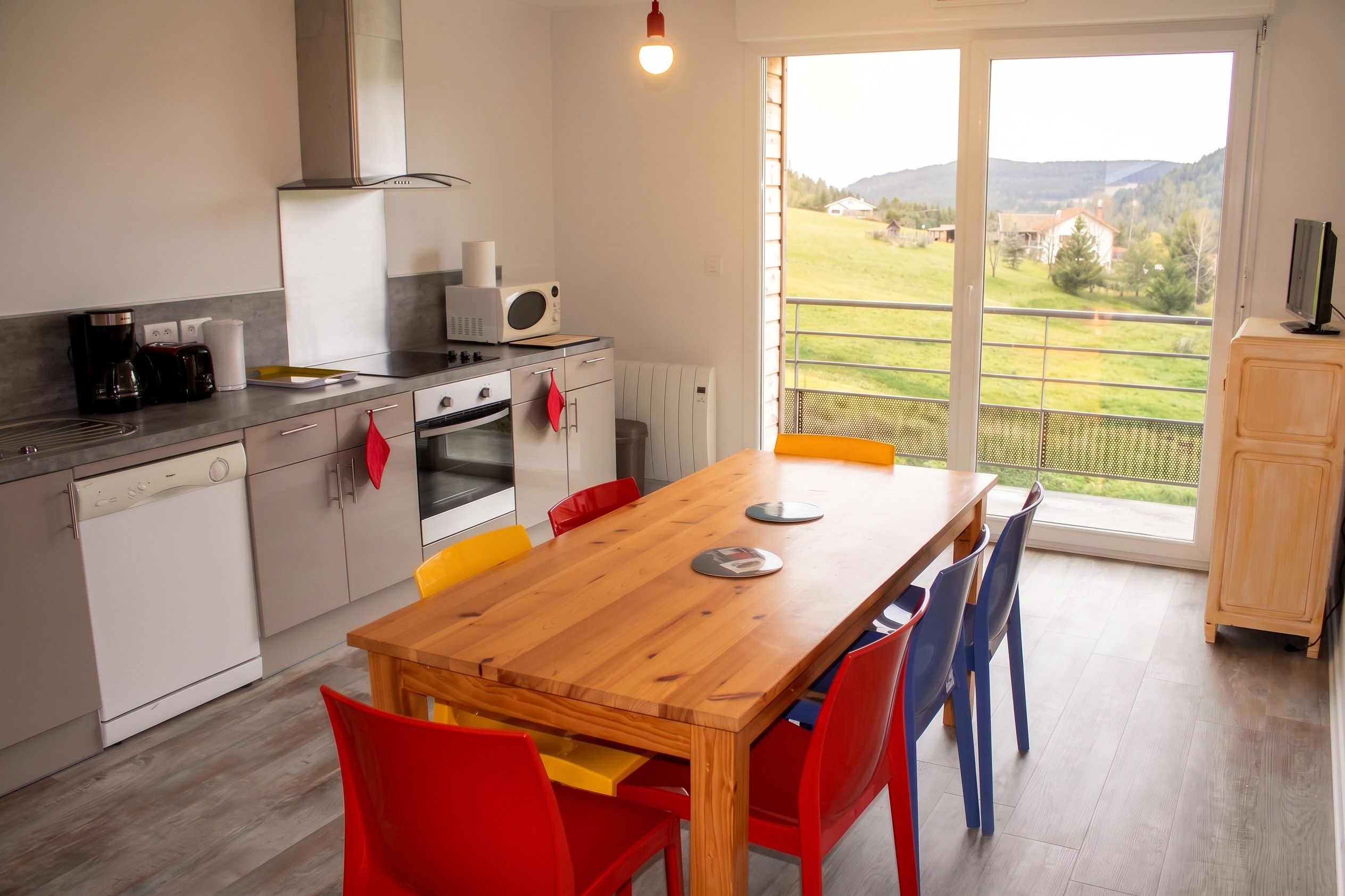 Een moderne keuken met een eethoek, uitzicht op een groen landschap en een televisie op een kast.