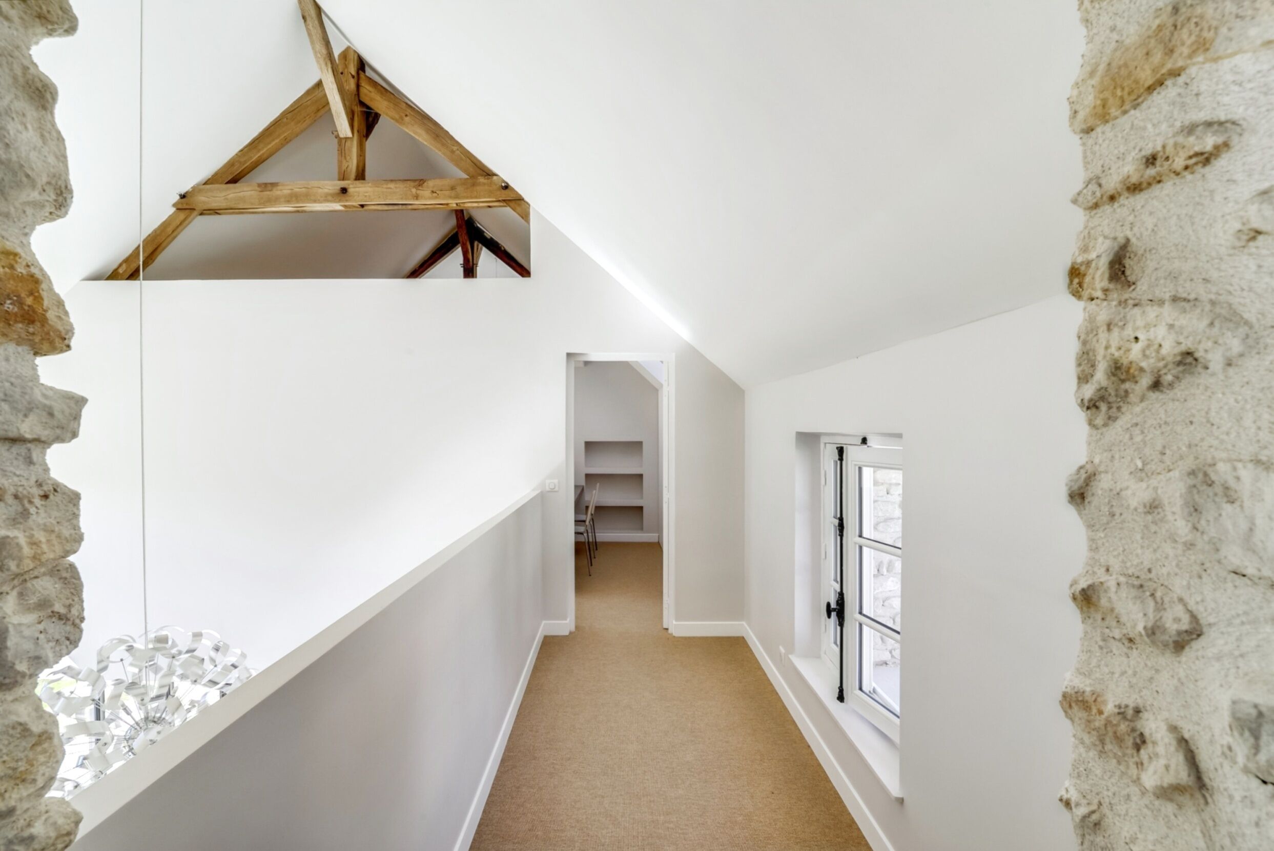 A narrow hallway with white walls, a wooden ceiling, and a carpeted floor.