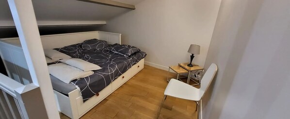 Une petite pièce bien éclairée, avec un lit superposé, un bureau avec une chaise et une lampe.