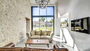 Ein modernes Wohnzimmer mit Steinwand, großem Fenster, einem beigefarbenen Sofa, einem braunen Ledersessel und einem Holztisch.