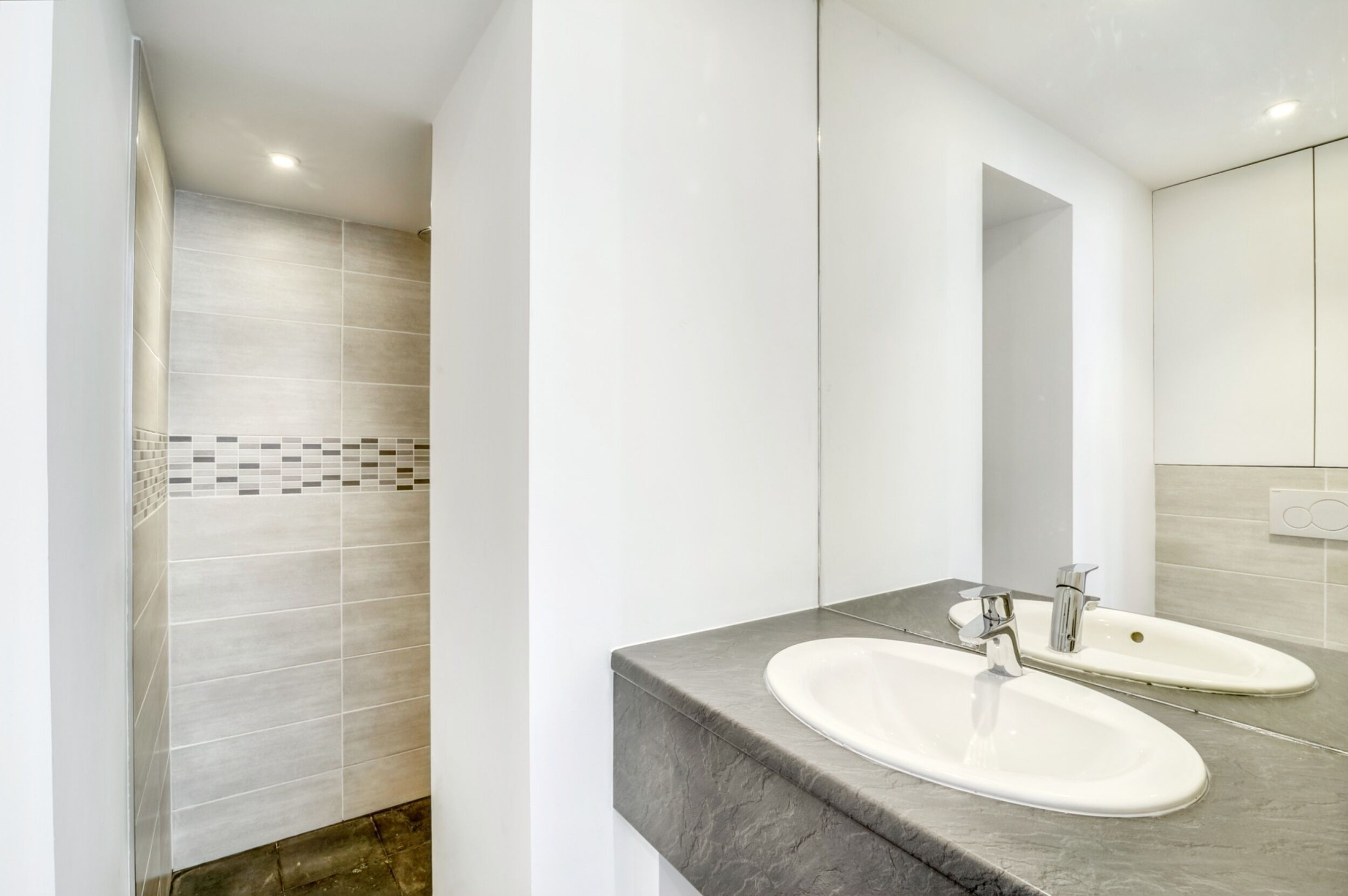 A modern bathroom with two sinks, a large mirror, and a shower area with tiled walls.
