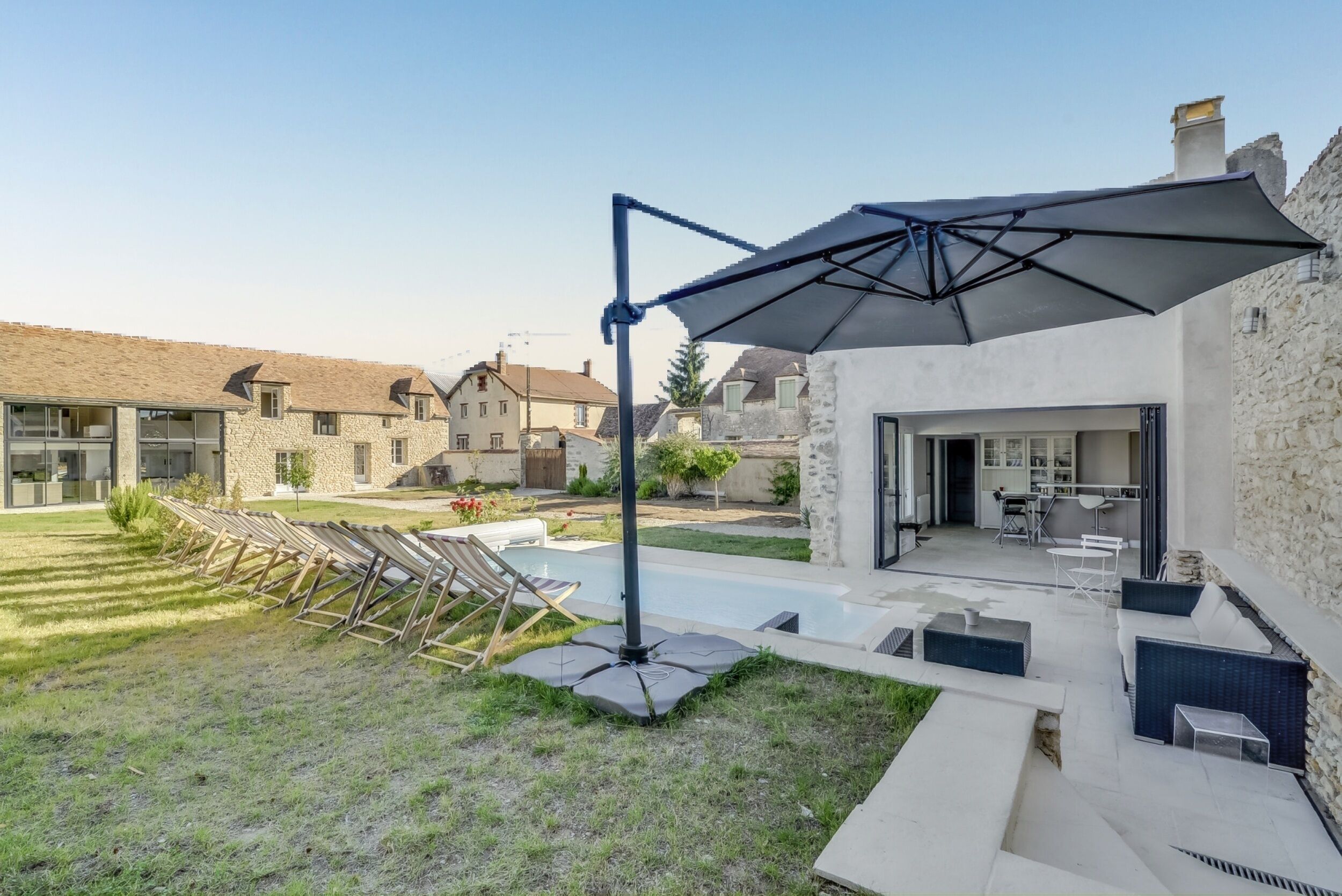 Een modern terras buiten met een zwembad, lounge fauteuils en een overdekte zithoek.