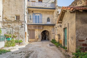 A narrow alleyway with a stone building featuring an arched entrance, a wooden balcony, and a small window with shutters. - Homerez - Charming Studio in Villeneuve, 45m², balcony (Villeneuve-lès-Avignon)