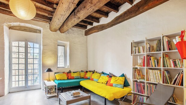 A living room with a yellow sectional sofa, a bookshelf, and a coffee table. - Homerez - Charming Studio in Villeneuve, 45m², balcony (Villeneuve-lès-Avignon)
