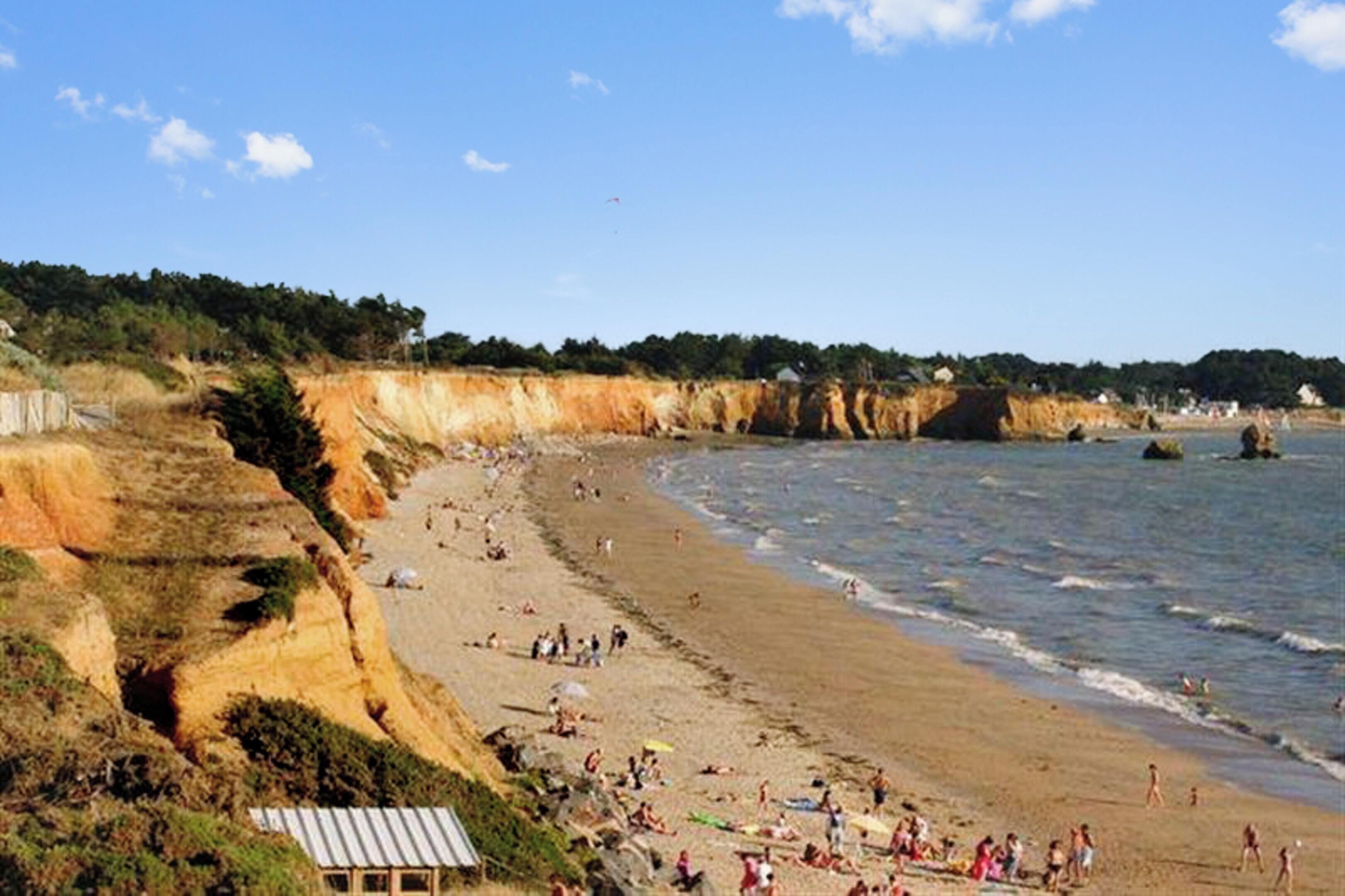 A beach with people, cliffs, and a small building.