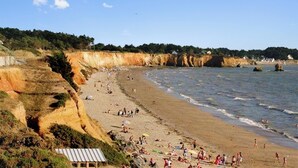 Une plage avec des gens, des falaises et un petit bâtiment.