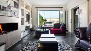 A modern living room with a fireplace, a red sofa, a black leather armchair, and a view of a pool and buildings through large glass doors. - Exceptional Master House  et  Mooring (PORT GRIMAUD)