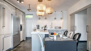 A modern kitchen with stainless steel appliances, a central island with seating, and pendant lighting. - Exceptional Master House  et  Mooring (PORT GRIMAUD)
