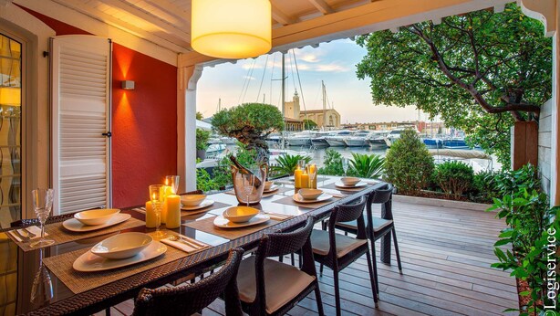 An outdoor dining area with a view of the marina, a table set with plates and candles, and a hanging light fixture. - Exceptional Master House  et  Mooring (PORT GRIMAUD)