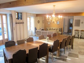 A spacious dining area with a long wooden table and multiple chairs, a chandelier, and a cozy seating area with a sofa and chairs in the background.