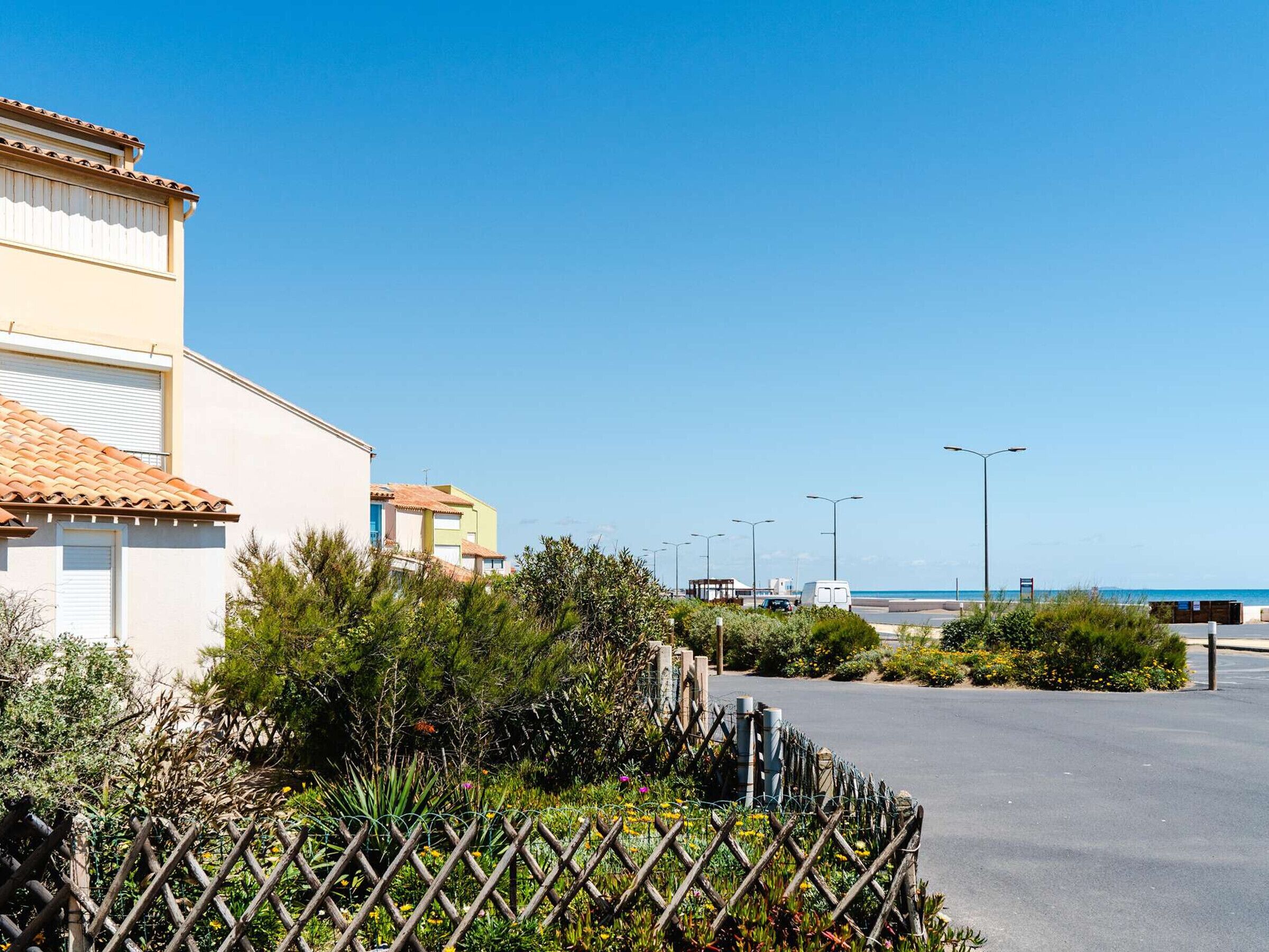 Um edifício costeiro com telhado de azulejos, rodeado por vegetação e um céu azul límpido.