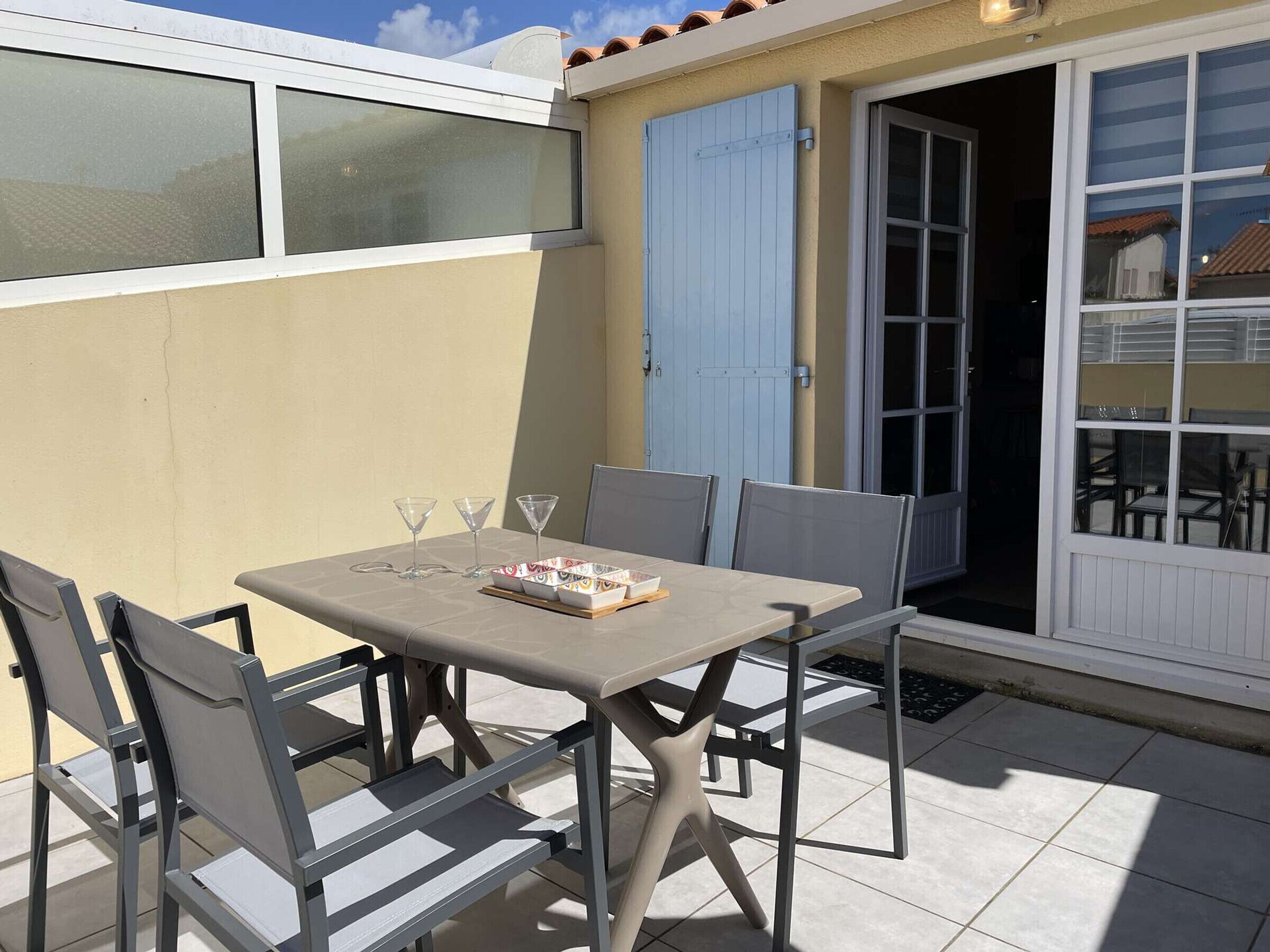 Eine Terrasse mit Tisch und Stühlen, einer Schiebetür und einem Fenster mit Blick auf eine Wohngegend.