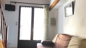 A living room with a sofa, a television mounted on the wall, and a sliding glass door. - Cozy 2-Bedroom Villa + Mezzanine, Sleeps 6, Steps to Beach, Parking, TV, Washer (Port Leucate)