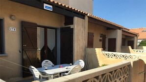 A building with a sign reading "CLEVACANCES" and the number 271. There is a patio area with a table and chairs, a decorative fence, and a door with a window. - Cozy 2-Bedroom Villa + Mezzanine, Sleeps 6, Steps to Beach, Parking, TV, Washer (Port Leucate)