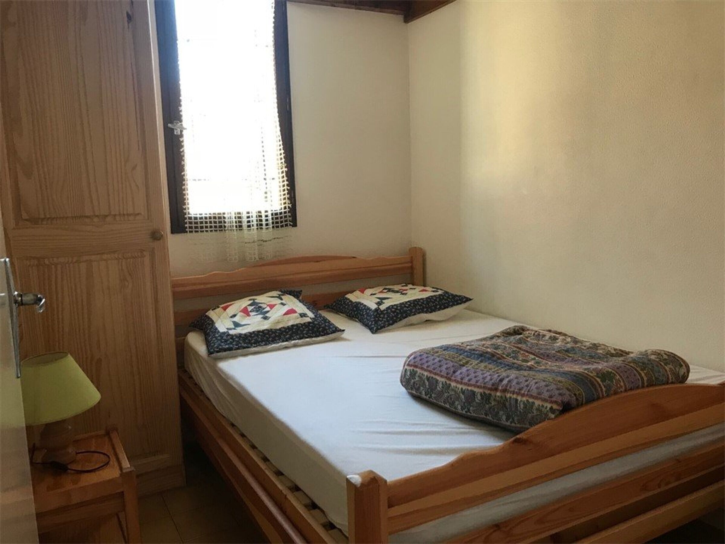 Un lit simple avec une tête de lit en bois, deux oreillers et une couverture à motifs.