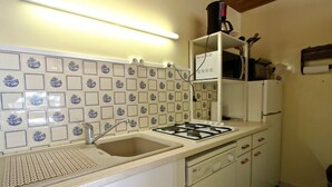A kitchen with a gas stove, sink, and white cabinets. There is a white refrigerator and a coffee maker on the counter.