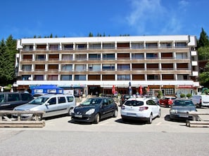 A multi-story hotel with a central entrance, several balconies, and a parking lot with various cars.