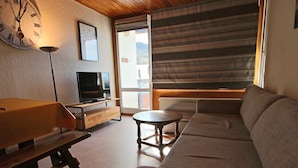 A living room with a sofa, a TV, a wooden table, and a clock on the wall.