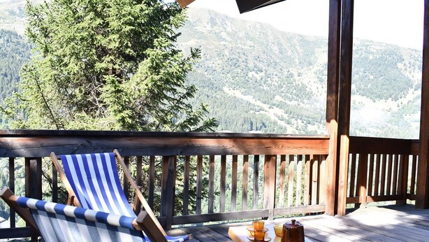 A wooden deck with a blue-striped lounge chair and a small table with a teapot and cups.