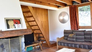 A cozy living room with a wooden staircase, a sofa, a TV, and a stone fireplace.